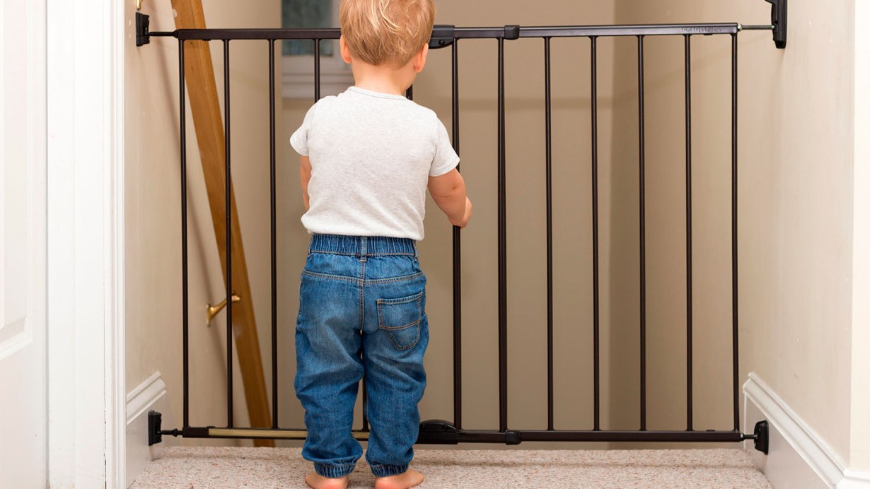 A toddler looking down the stairs through a baby gate